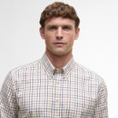 A man with short hair wears a buttoned, multicoloured plaid shirt against a plain white background, conveying a clean, casual look.