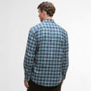 A man stands with his back to the camera, wearing a blue and green plaid shirt. The setting is a simple, neutral background, conveying a casual tone.