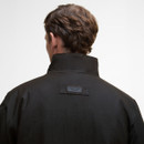 Rear view of a person with brown hair wearing a high-collared dark jacket. A label with the brand name is visible, conveying a sleek and modern tone.