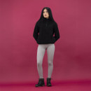 Full body view of woman wearing black fleece pullover, light grey ribbed leggings and black ankle boots with knit collar, standing against dark pink backdrop.