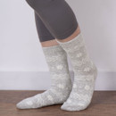 Person wearing light grey ankle socks with white Fair Isle snowflake pattern, standing on a wooden floor with legs crossed.