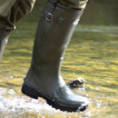 Close-up of olive green Grisport wellington boots splashing through shallow stream water, with droplets caught mid-air and sunlight reflecting off the wet boot surface.