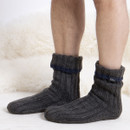 A person wearing dark grey ribbed knit thermal bed socks with rolled cuffs and a navy stripe detail. The socks feature a small 'Totes' label and are shown against a cozy white faux fur background.