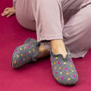 Person seated on a magenta floor wearing grey felt slippers adorned with bright polka dots in orange, pink, and lime green; paired with light mauve pyjama trousers. Person seated on a magenta floor wearing grey felt slippers adorned with bright polka dots in orange, pink, and lime green; paired with light mauve pyjama trousers.