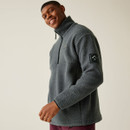 A man smiling and looking to the side while wearing a grey fleece pullover with a high collar and half-zip front. The fleece features a chest logo and a branded patch on the sleeve.