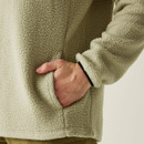 Close-up of the beige fleece’s side pocket with a hand partially inserted, showing the soft fleece texture and neatly finished edges.