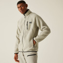 Model wearing the zipped Abbey Stone fleece jacket, standing in a relaxed pose with one hand in the side pocket, showing the front pocket layout and logo.