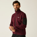Male model showcasing the NEWHILL fleece jacket in dark maroon, zipped up with hands adjusting sleeves, emphasizing comfort and style.