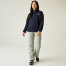 Full-body shot of the model walking forward in the navy fleece and light mint-green trousers, showcasing the garment's casual outdoor look.