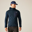 Front view of a male model wearing the Regatta Hooded Newhill Full Zip Fleece in Moonlight Denim, styled with black outdoor trousers and a navy cap, standing against a neutral indoor backdrop.