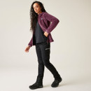 A full length view of a woman wearing a purple fluffy fleece with black trousers and walking boots.