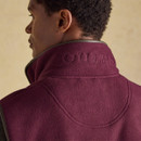 Rear close-up of a man wearing a burgundy-coloured fleece gilet with brown trim, featuring the word "JOULES" subtly embroidered across the back of the high collar.