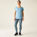 A full length view of a woman wearing a light blue v-neck t-shirt with blue leggings and trainers.