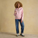 Full-length view of a woman in a pink and white striped hoodie paired with blue cuffed jeans and green trainers, standing casually against a neutral background.