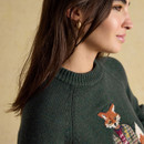 Detailed view of the ribbed crew neckline of the green jumper and the playful fox embroidery in a tweed jacket and fair isle vest.