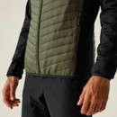 A person wearing a green quilted jacket with black sleeves and trousers. The focus is on the jacket's texture and zippered pockets. The tone is casual and functional.