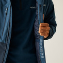 A person wearing a blue Regatta outdoor jacket, partially unzipped to reveal inner labels with environmental icons. The tone is practical and informative.