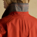 Close-up of the back of a red women’s field jacket, featuring a raised collar lined with a checked pattern in navy, beige, and red. The word 'JOULES' is embroidered across the back of the collar in matching red thread. Neat seam detailing runs down the centre back, with a subtle stitched triangle motif below.