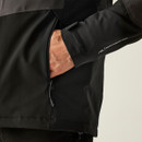 A close-up of a person’s hand in the pocket of a black jacket. The sleeve shows "Isotex Stretch 15000," implying waterproof and flexible fabric.
