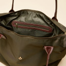 Close-up view of the inside of a women’s olive green tote bag, showing a spacious compartment with a zip closure. The inner lining is dark olive with a subtle dotted pattern and features a built-in zip pocket trimmed with brown faux leather.
