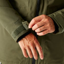 Close-up of hands adjusting the velcro cuff of a green Isotex jacket, highlighting the texture and functionality of the waterproof material.