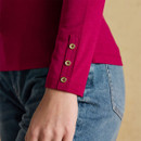 Detail shot of a berry-coloured long-sleeve top featuring three small gold buttons on the cuff, worn with high-waisted light blue jeans.