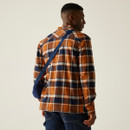 Man in a brown and navy plaid shirt with a blue crossbody bag, facing away. The setting is neutral, conveying a casual, relaxed vibe.