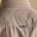 Close-up of the back yoke of a checked shirt in beige, burgundy, and navy, featuring the 'Joules' brand label stitched in blue below the collar seam.