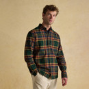 Male model wearing a Joules brushed cotton shirt in a bold forest green and ochre tartan check. The shirt features a classic collar, button-down front, and chest pocket with embroidered hare logo. Styled casually with cream corduroy trousers against a neutral studio backdrop.