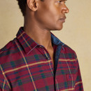 Side profile of a man wearing a red brushed cotton tartan shirt featuring a green, navy, and mustard check pattern, with the top button undone to reveal a denim-look inner collar.