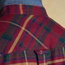 Close-up of the back of a red tartan shirt with green, navy, and mustard check pattern; denim-style inner collar visible, and a small blue 'Joules' brand tab stitched beneath the yoke.