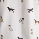 Close-up of fabric showing a whimsical all-over print of illustrated dogs in various poses and breeds, including terriers, labradors, and spaniels. The design appears on a soft white background, part of a printed shirt.
