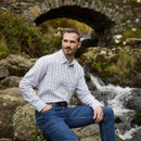 Men’s white check country shirt worn outdoors beside a rocky stream, styled with blue jeans for a classic rural look.