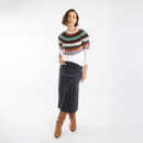 A full length view of a woman wearing a black denim skirt with brown boots and a white patterned jumper.