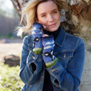 A woman in a denim jacket and colourful knit gloves poses by a tree, smiling gently. Her hair is windswept, creating a relaxed and cheerful tone.