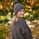 Woman in a cosy knit hat and sweater smiles warmly, looking back over her shoulder. Autumn leaves blur in the sunlit background, creating a serene mood.