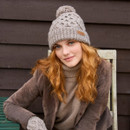 Relaxed seated pose in Enniskerry Bobble Beanie in Mushroom – Warm and stylish chunky-knit hat with bobble detail, paired with casual layered winter clothing for an outdoor-inspired lifestyle look.