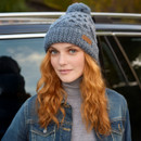 Relaxed front-side view of model in slate blue cable knit bobble beanie – Textured wool hat with ribbed fold-over cuff and branded patch, styled for outdoor winter comfort.