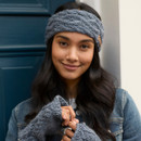 Front view of woman wearing a slate blue knitted headband with cable pattern, styled with loose wavy hair and casual grey top.