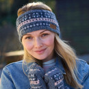 Woman wearing a slate blue Inveraray knitted headband with soft pink and white accents, smiling outdoors with matching knitted handwarmers.