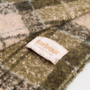 Close-up of a soft plaid fabric in shades of green and beige, featuring a "Barbour" label. The texture is cosy and inviting.