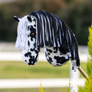 A black-and-white spotted hobby horse head with a black and white yarn mane, mounted on a wooden stick, against a blurred outdoor background with greenery.
