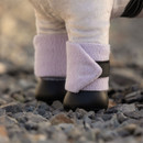 Close-up of a toy horse’s lower legs wearing light purple fleece bandages secured with black straps, standing on a gravel surface.