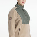 A woman wearing a beige fleece jacket with an olive green panel across the upper chest and shoulders, featuring a half-zip front and a high collar. The jacket has zip pockets and a round LeMieux logo patch on the upper sleeve, paired with burgundy riding leggings.