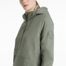 Woman wearing a sage green hooded anorak jacket with a half-zip front, large flap pocket, and drawstrings at the hood. The jacket has a circular "LeMieux" logo patch on the upper sleeve and a relaxed fit, paired with matching sage green leggings.