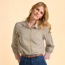 A woman with long blonde hair wears a striped shirt and jeans, against a light beige background, looking relaxed and confident.