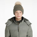 Woman wearing a khaki green ribbed knit beanie with a beige faux fur pom pom, paired with a matching khaki padded jacket, by LeMieux.