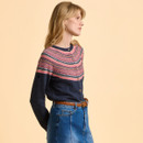 Woman in a navy and pink patterned cardigan and denim skirt, standing against a beige background. She looks to the side with a neutral expression.