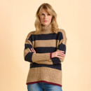 A woman in a cosy, striped turtleneck sweater poses against a light beige background. Her expression is neutral, arms crossed, wearing blue jeans.