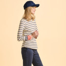 Woman in a navy cap and striped jumper with red cuff accents, standing against a soft beige background. She appears relaxed and content.